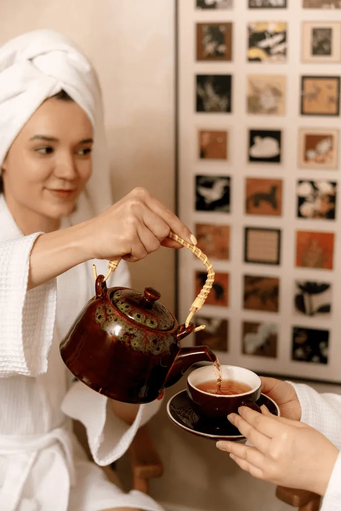 Guest at ApaThai Almaty pouring warm herbal tea for her friend in a relaxing Thai spa atmosphere.