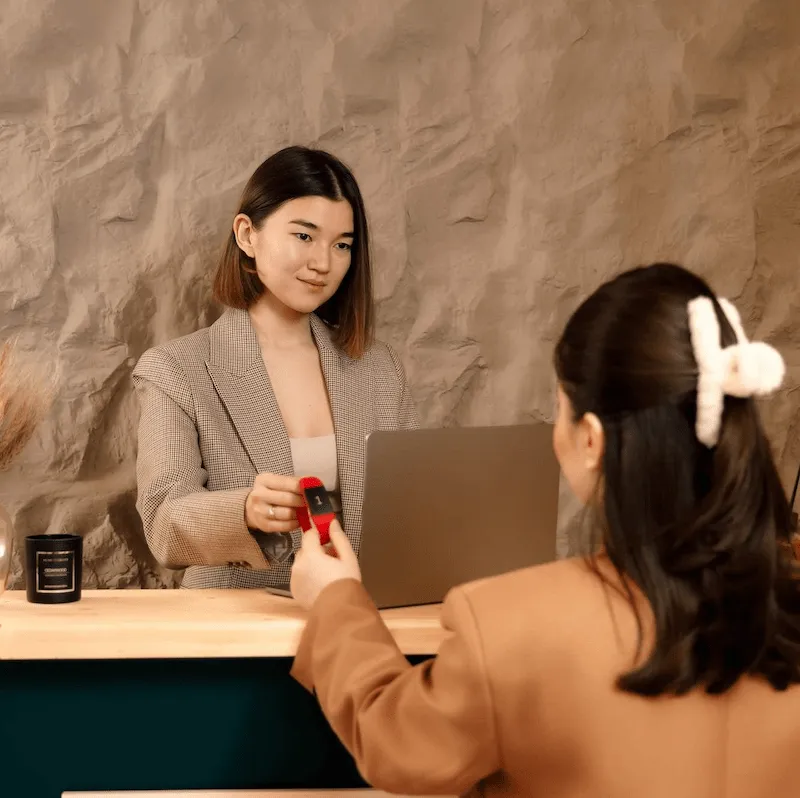 Receptionist at ApaThai Almaty processing a guests payment at the front desk in a warm, welcoming spa environment.